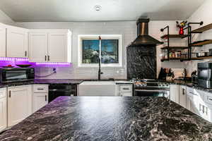 Kitchen with wall chimney range hood, stainless steel gas range, sink, and white cabinets