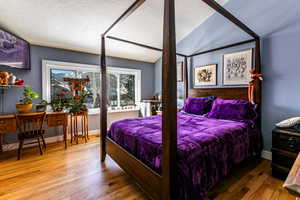 Bedroom with wood-type flooring, lofted ceiling, and a textured ceiling