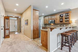 Kitchen with a kitchen breakfast bar, decorative backsplash, light colored carpet, kitchen peninsula, and stainless steel appliances