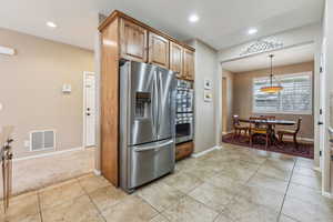 Kitchen with pendant lighting, light colored carpet, and appliances with stainless steel finishes