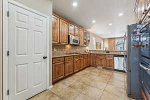 Kitchen featuring appliances with stainless steel finishes, sink, decorative backsplash, light tile patterned floors, and light stone counters