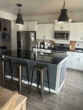 Kitchen featuring appliances with stainless steel finishes, a kitchen breakfast bar, decorative light fixtures, and white cabinets