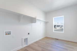 Clothes washing area featuring hookup for a washing machine, electric dryer hookup, and light hardwood / wood-style floors