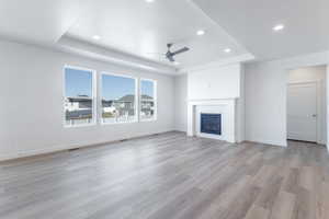 Unfurnished living room with a tiled fireplace, a tray ceiling, light hardwood / wood-style floors, and ceiling fan