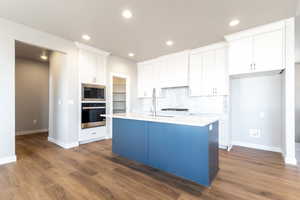 Kitchen with a kitchen island with sink, white cabinetry, built in microwave, and oven