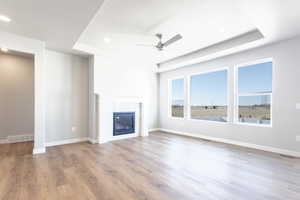 Unfurnished living room featuring a raised ceiling, ceiling fan, and light wood-type flooring