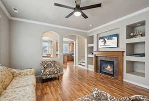 Living room with hardwood / wood-style floors, built in shelves, ornamental molding, and a tile fireplace