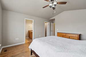 Bedroom with lofted ceiling, ensuite bath, ceiling fan, light hardwood / wood-style floors, and a walk in closet