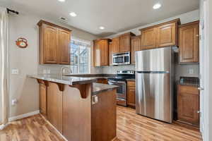 Kitchen featuring a breakfast bar, stainless steel appliances, kitchen peninsula, and light hardwood / wood-style flooring