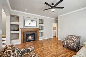 Living room with crown molding, hardwood / wood-style flooring, independent washer and dryer, a tiled fireplace, and built in shelves