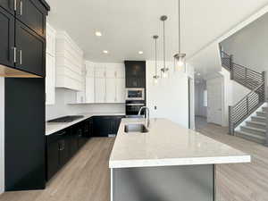 Kitchen featuring sink, appliances with stainless steel finishes, hanging light fixtures, tasteful backsplash, and an island with sink