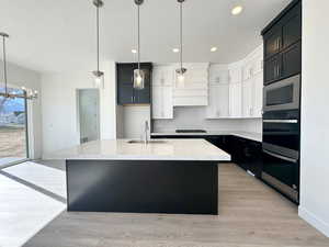 Kitchen with stainless steel microwave, decorative light fixtures, white cabinetry, an island with sink, and sink