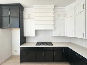 Kitchen with white cabinetry, backsplash, light stone counters, and stainless steel gas stovetop