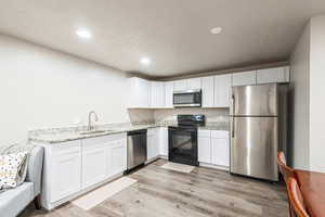 Kitchen featuring appliances with stainless steel finishes, sink, white cabinets, and light wood-type flooring