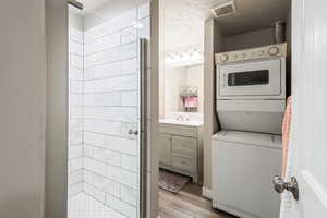 Laundry room with stacked washer and clothes dryer, sink, a textured ceiling, and light wood-type flooring