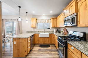 Kitchen with sink, light stone counters, hanging light fixtures, kitchen peninsula, and stainless steel appliances