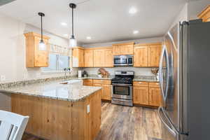 Kitchen featuring sink, hardwood / wood-style flooring, hanging light fixtures, kitchen peninsula, and stainless steel appliances