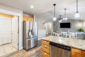 Kitchen featuring stainless steel appliances, light stone counters, decorative light fixtures, vaulted ceiling, and light wood-type flooring