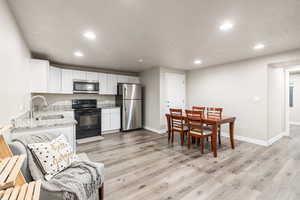 Kitchen with white cabinetry, sink, light stone counters, stainless steel appliances, and light hardwood / wood-style flooring