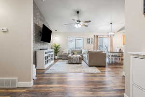 Living room featuring vaulted ceiling, ceiling fan with notable chandelier, and dark hardwood / wood-style flooring