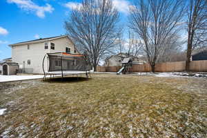 Yard covered in snow featuring a trampoline and a playground