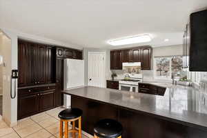 Kitchen with sink, white appliances, light tile patterned floors, a kitchen breakfast bar, and kitchen peninsula