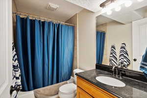 Full bathroom featuring vanity, shower / bathtub combination with curtain, a textured ceiling, and toilet