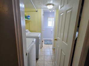 Washroom with light tile patterned flooring, washer and dryer, and a textured ceiling