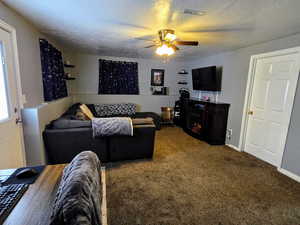 Living room featuring ceiling fan, carpet, and a textured ceiling