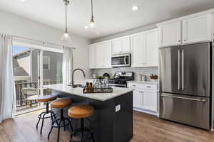 Kitchen with stainless steel appliances, an island with sink, white cabinets, and decorative light fixtures