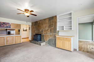 Unfurnished living room featuring a wood stove, light carpet, and ceiling fan