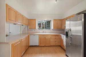 Kitchen featuring sink, stainless steel fridge, white dishwasher, kitchen peninsula, and light hardwood / wood-style flooring