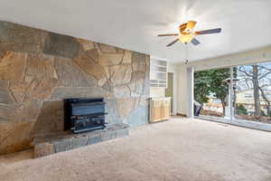 Unfurnished living room featuring a wood stove, ceiling fan, and carpet