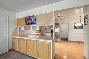 Kitchen with stainless steel refrigerator with ice dispenser, an inviting chandelier, light wood-type flooring, kitchen peninsula, and black electric stovetop