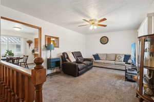 Living room with a textured ceiling, ceiling fan, and carpet