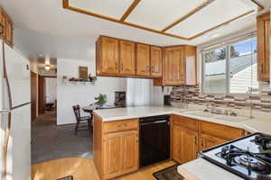 Kitchen with black dishwasher, sink, decorative backsplash, white fridge, and kitchen peninsula