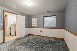 Empty room featuring washer / clothes dryer, carpet, and a textured ceiling