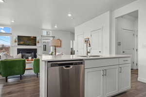 Kitchen featuring white cabinetry, dishwasher, sink, a kitchen island with sink, and a brick fireplace