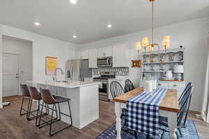 Kitchen with sink, an island with sink, pendant lighting, stainless steel appliances, and white cabinets