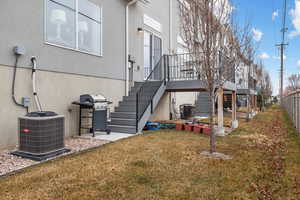 Back of property with a wooden deck, a lawn, and central air condition unit