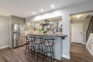 Kitchen featuring a breakfast bar, island range hood, butcher block countertops, stainless steel appliances, and dark wood-type flooring