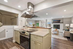 Kitchen featuring stainless steel electric stove, island range hood, a fireplace, a center island, and dark wood-type flooring