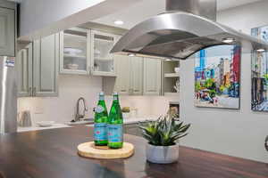 Kitchen featuring tasteful backsplash, island range hood, sink, and gray cabinetry