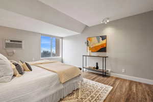 Bedroom with wood-type flooring, vaulted ceiling, a baseboard heating unit, and a wall mounted air conditioner