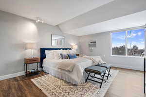 Bedroom featuring lofted ceiling, hardwood / wood-style floors, and a wall unit AC