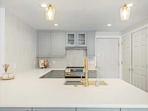 Kitchen featuring pendant lighting, stainless steel range, gray cabinetry, and kitchen peninsula