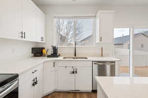 Kitchen with dark hardwood / wood-style floors, sink, white cabinets, light stone counters, and stainless steel appliances