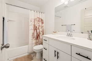 Full bathroom with vanity, shower / bathtub combination with curtain, and toilet