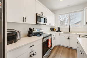 Kitchen featuring sink, stainless steel appliances, light stone counters, light hardwood / wood-style floors, and white cabinets