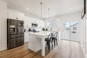 Kitchen with stainless steel appliances, white cabinetry, a kitchen island, and a breakfast bar